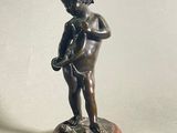 une petite statue représentant un garçon tenant un oiseau, posée sur un socle en bois