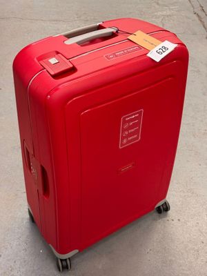 une valise rouge posée par terre, sur laquelle est accrochée une étiquette de prix