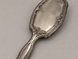 an antique silver plated mirror with a handle on a white surface