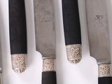 several knives are lined up on a white surface with a black handle