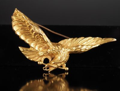 une image représentant une broche en forme d'oiseau doré posée sur une surface noire