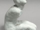 a white sculpture of a man sitting on his knees on a gray surface