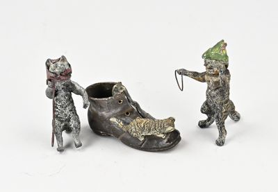 trois figurines de chats et une chaussure posées sur une surface blanche