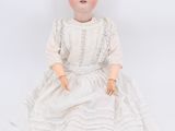 an old doll sitting on a white surface wearing a white dress