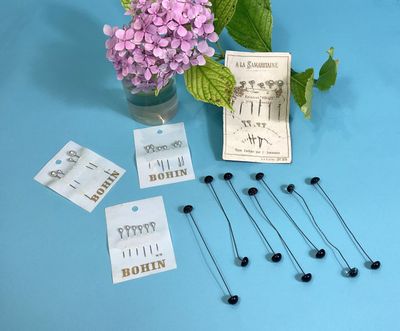 some pins and flowers in a vase on a blue table