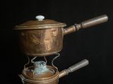une petite casserole en cuivre avec une poignée en bois sur fond noir