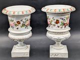 pair of white vases with floral designs on them sitting on a stand