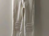 white jeans with zippers hanging on a hanger against a wall