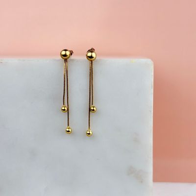 a pair of gold earrings sitting on top of a marble block