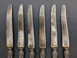five antique silverplated knives are lined up on a black surface