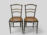 a pair of black and gold painted chairs with cane seats