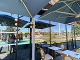 des tables et des chaises sous des parasols, sur une terrasse avec une piscine en arrière-plan