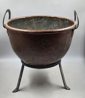 une grande casserole en métal posée sur un support et munie d'une poignée