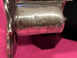 a silver clock on a stand on a pink surface