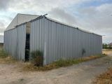 un grand bâtiment métallique dont la porte est ouverte, donnant sur un chemin de terre