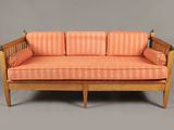 un canapé rayé orange, avec une structure en bois et des accoudoirs, sur fond gris