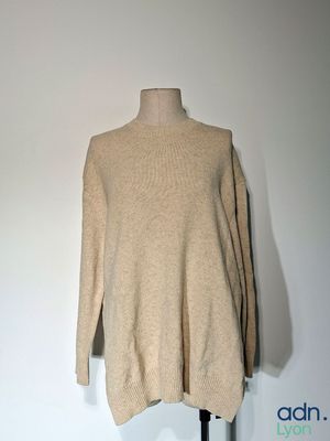 un pull à col roulé beige sur un mannequin posé contre un mur blanc