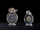 two small glass clocks with birds on them on a table