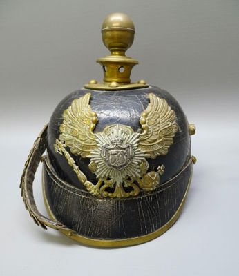 un vieux casque orné d'un aigle doré, posé sur une surface blanche