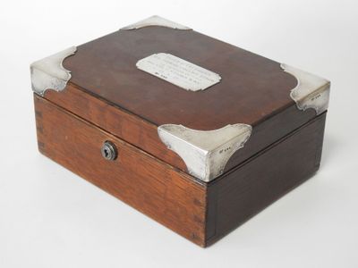 une petite boîte en bois avec un couvercle en métal, posée sur une surface blanche