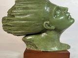une sculpture verte représentant la tête d'une femme, posée sur un socle en bois