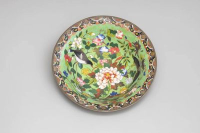 une assiette verte sur laquelle sont peints des fleurs et des oiseaux