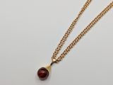 a gold plated necklace with a red stone on a chain