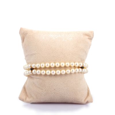 des bracelets de perles posés sur un coussin, sur fond blanc