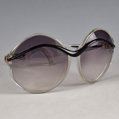 une paire de lunettes de soleil posée sur une surface blanche, sur fond gris