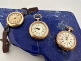trois types différents de montres de poche posées sur une dalle de pierre bleue