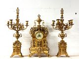 trois bougeoirs dorés et une horloge posés sur une étagère