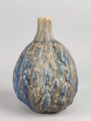 un vase bleu et brun posé sur une surface blanche