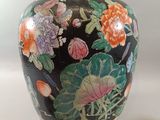 a black vase with flowers on it next to a remote control