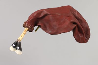 une main tenant un pinceau et un sac suspendu à une ficelle