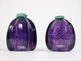 une paire de vases en verre violet avec des couvercles verts, posés sur une surface blanche