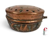 a small copper pot with holes in it on a white surface