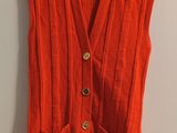an orange sweater vest hanging on a wall next to a hanger