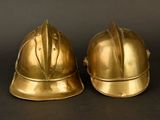 pair of antique brass fire helmets on a black background