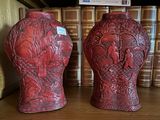 deux vases rouges posés sur une étagère devant des livres