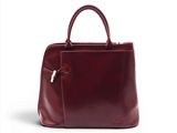 Le sac à main en cuir bordeaux est posé sur une surface blanche.