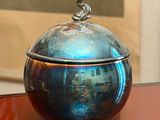 a silver bowl sitting on a table with a picture in the background