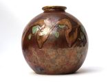 a brown vase with green leaves on it on a white surface