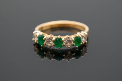 un gros plan d'une bague en or sertie de pierres vertes sur un fond noir