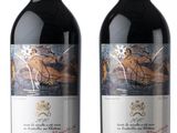 two bottles of red wine sitting next to each other on a white surface