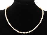 un collier de perles blanches autour du cou d'un mannequin, muni d'un fermoir en or