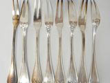 six forks and a knife are lined up on a white surface
