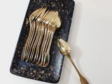 a black plate with gold forks and spoons on it