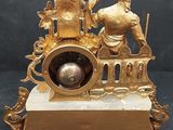 a gold clock with a man and a woman sitting on it