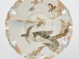 une assiette ornée d'un oiseau, posée sur un socle