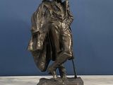 bronze statue of a man with a hat and coat holding a cane